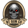 A dark-themed logo with a central detailed skull featuring one red eye and a target graphic in the other socket. Surrounding the skull is a circular emblem labeled "EST. 2023" on the sides. The bottom has a banner reading "BT GUN CO" and the URL "WWW.BTGUNCO.COM.