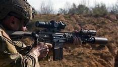 US Army soldier aiming a modern carbine rifle during field testing.