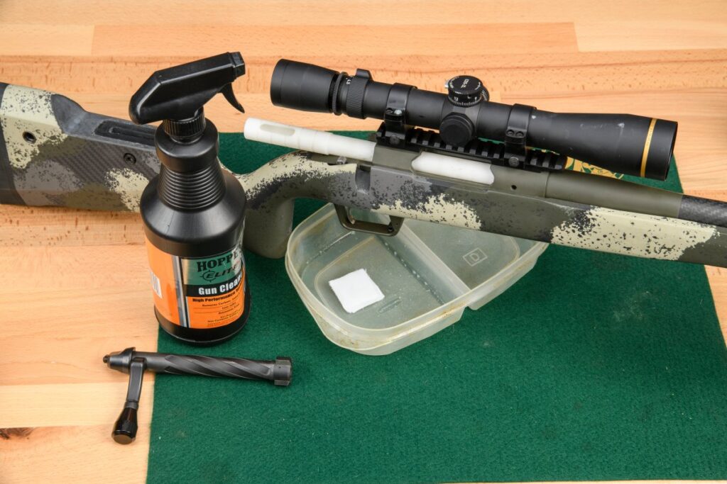 A person cleaning a bolt action rifle with a bore brush and solvent