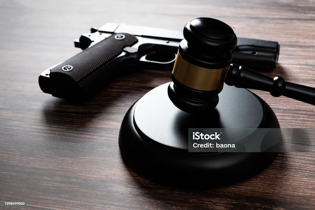 A wooden judge gavel resting next to a modern handgun, representing legal firearm regulations