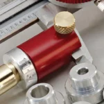 Hornady Lock-N-Load Comparator Body, red metal body with brass knob and silver inserts close-up