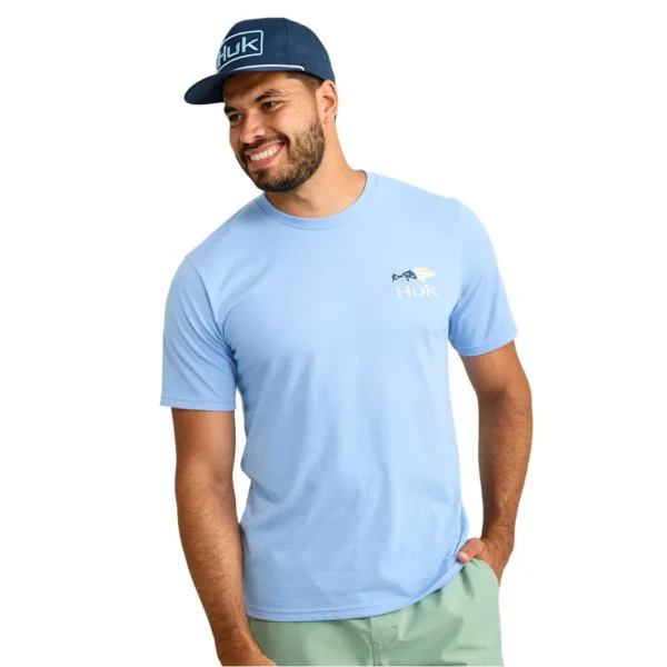 Huk Fish Flag Short Sleeve Shirt, front view in Marolina blue worn by a man with a blue cap