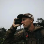 Leupold RX-5000 TBR/W Range Finder with DNA, black, held to a man's eye outdoors