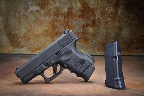 primary-26277 Pachmayr PKMYR GRIP EXTENDER FOR GLK 26 +XL black pistol beside an upright magazine