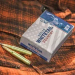 Nosler Whitetail Country, blue and white ammunition box with brass cartridges on plaid fabric