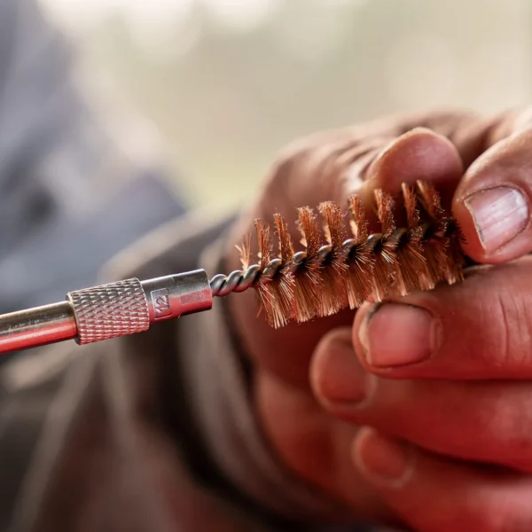 SHOOTERS CHOICE 12GA CLEANING KIT, close-up of hands holding a bronze bore brush and cleaning rod