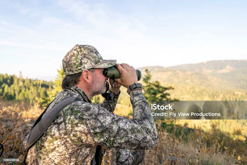 Hunter using binoculars to scan open terrain during a daylight hunt